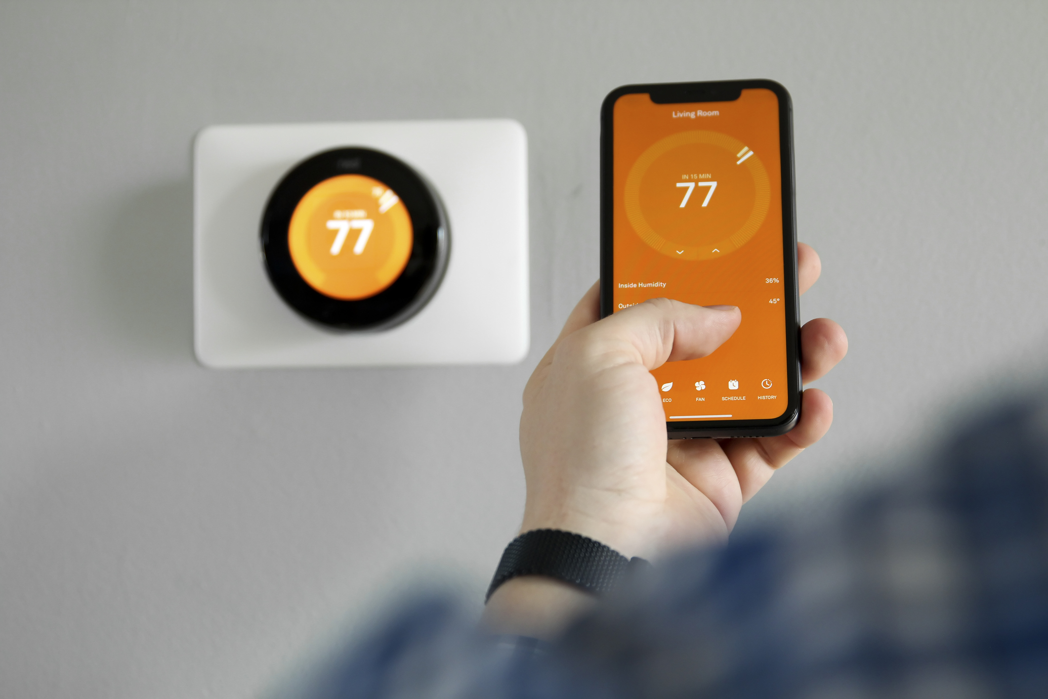 A phone controls the thermostat on the wall.